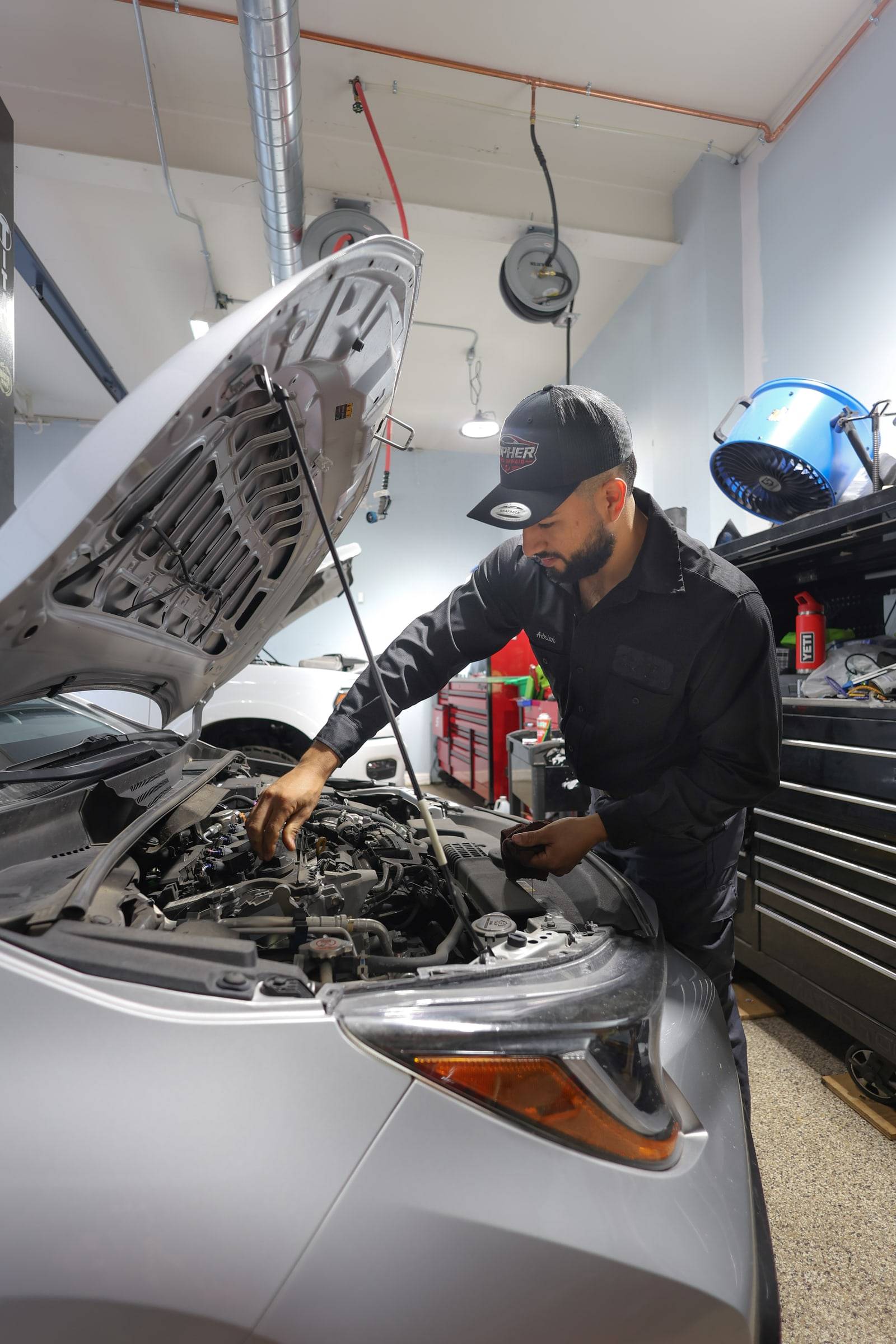 The lead tech leaning into the engine bay of a sedan with the hood up