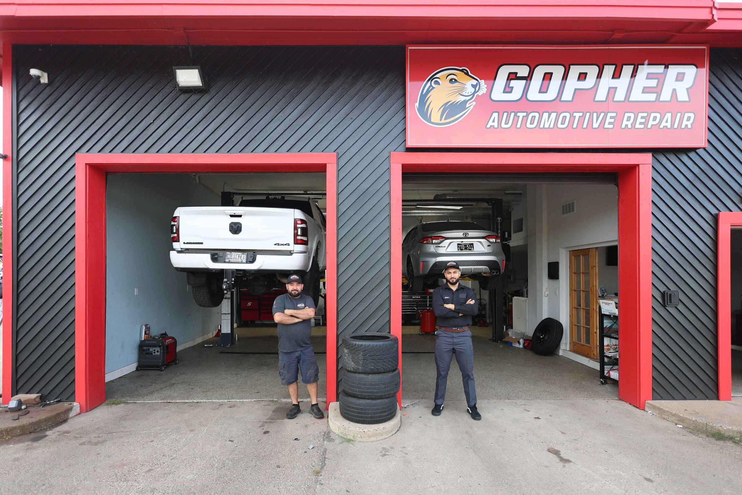 The owner and the lead tech standing with their arms crossed in front of the two open bays, under the red Gopher sign